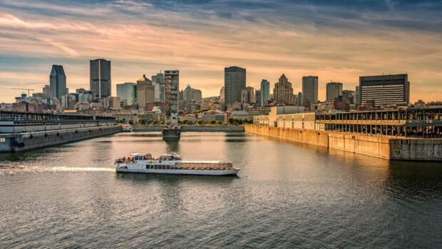 A boat cruises on the St Lawrence River with a city skyline under a golden sunset