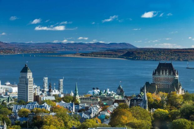 A panoramic view of the St Lawrence River with historic buildings and autumn foliage under a clear blue sky