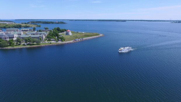 A scenic view of the St Lawrence River with a boat near a small island and buildings on a clear day