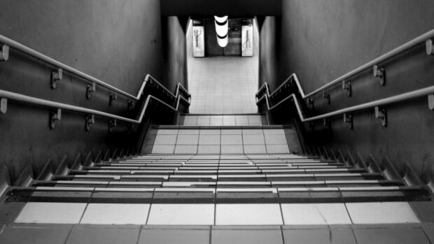 A tiled staircase with handrails going down in a monochrome setting