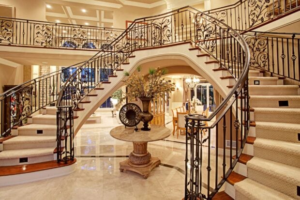 Elegant staircase with intricate iron railing and carpeted steps in a luxurious home interior