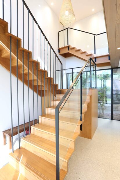 Modern wooden staircase with metal and glass railing in bright interior