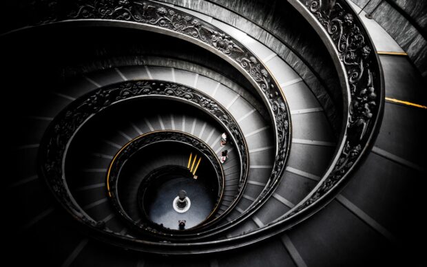 Spiral staircase with ornate railings viewed from above showing intricate details and people walking