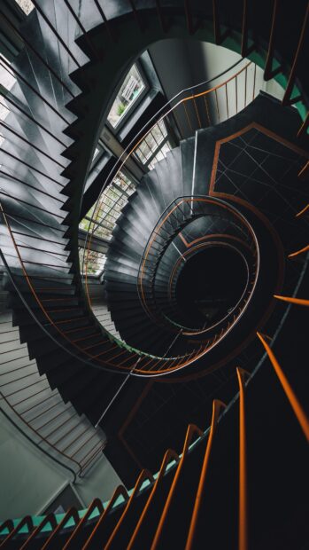 Spiral staircase with orange rails viewed from above in a dark building interior