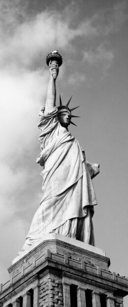 The Statue of Liberty stands tall with its torch against a cloudy sky in this photo, 2K Phone Wallpaper