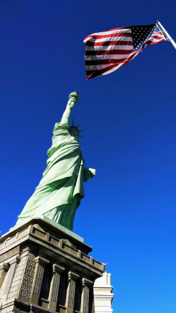 The Statue of Liberty stands tall under a clear blue sky with the American flag flying, HD Phone Wallpaper
