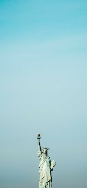 The Statue of Liberty holding a torch stands tall under a clear blue sky, 2K Mobile Wallpaper