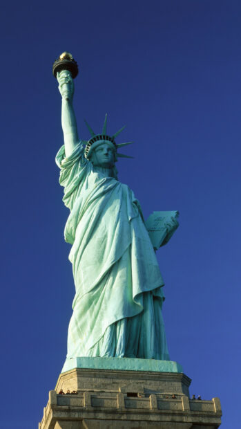 The Statue of Liberty holds a torch and a tablet under a clear blue sky, 2K Phone Wallpaper