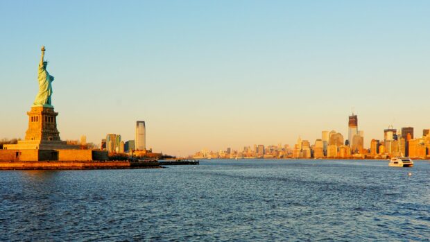 The Statue of Liberty stands tall overlooking the river with the city skyline in the background, 4K Desktop Wallpaper