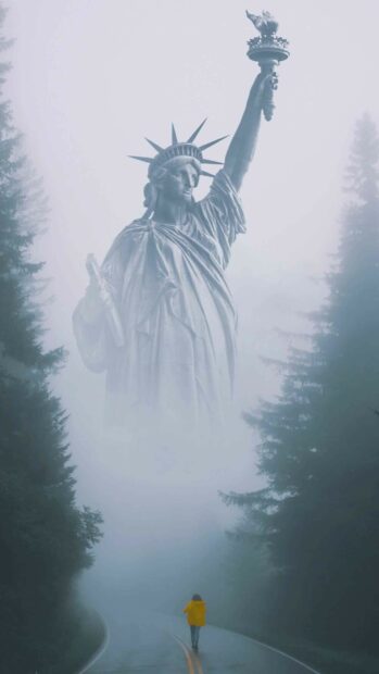 A person walks on a misty road beneath the Statue of Liberty surrounded by trees, 2K Phone Wallpaper