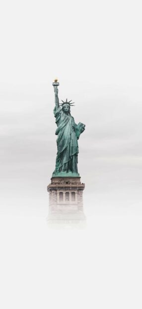 The Statue of Liberty stands tall above the mist with a cloudy backdrop, 2K Phone Wallpaper