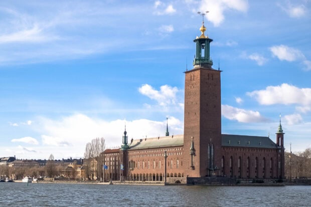 A historic Stockholm building with a tall tower beside the water under a blue sky