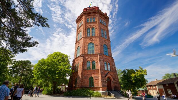 Historic Stockholm brick tower surrounded by trees and people walking on a sunny day