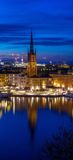 Nighttime cityscape of Stockholm with illuminated buildings and church tower reflected in the water