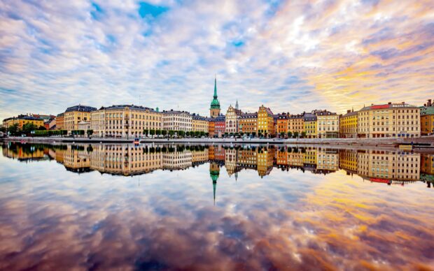 Colorful buildings in Stockholm reflect on calm water under a cloudy sky during sunset