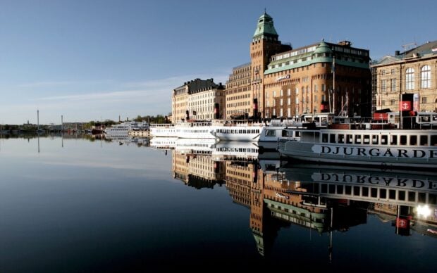 Historic buildings in Stockholm reflecting on calm water with boats docked along the quay