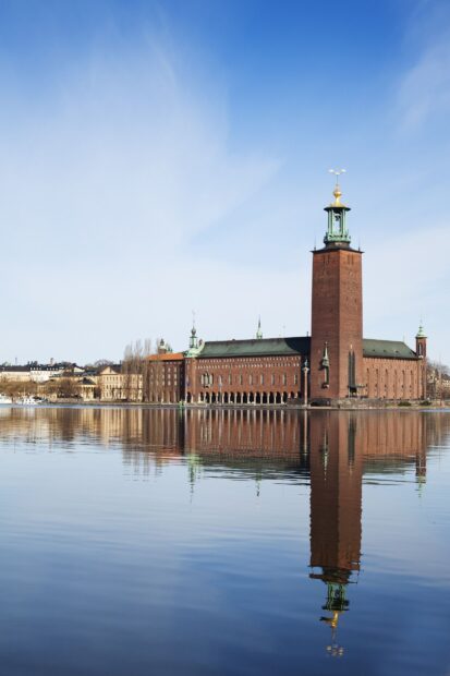 The historic Stockholm city hall reflected on calm water under a clear blue sky