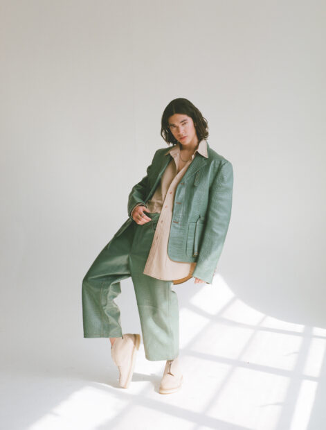 A person wearing a green textured suit and beige shoes posing in natural light with Conan Gray Wallpapers, 2K Mobile Wallpaper