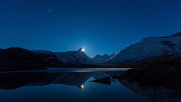 The sunlight shines over a snowy mountain lake reflecting on calm water at night with stars, 4K Desktop Wallpaper