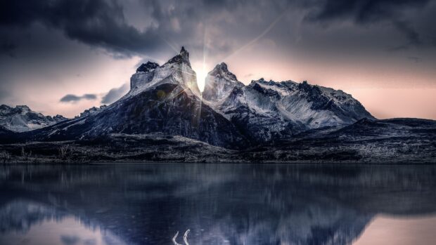 A serene mountain lake reflects jagged peaks with sunlight shining behind, 4K Desktop Wallpaper
