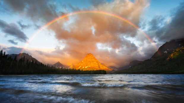 A vibrant mountain glows at sunset under a rainbow in Glacier National Park, 2K Desktop Wallpaper