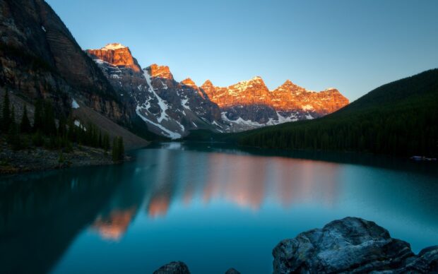 Sunset light warms the mountain lake surrounded by pine trees and rocky cliffs, 2K Desktop Wallpaper