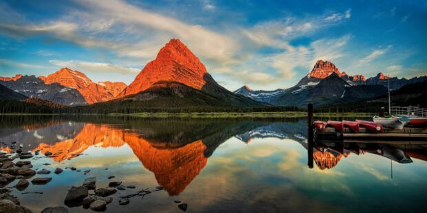 The vibrant sunset lights up Glacier National Park mountains with calm lake reflections, 2K Desktop Wallpaper