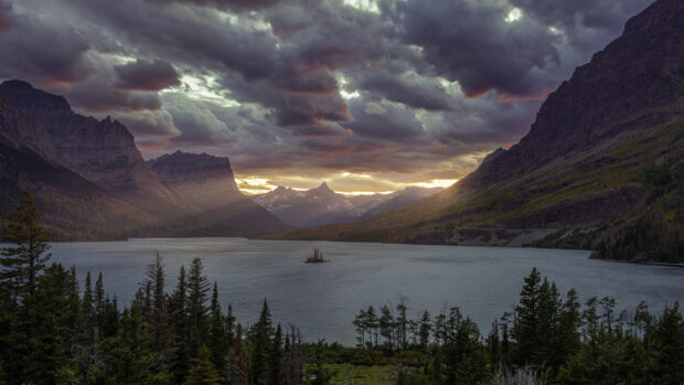 The sun sets behind dramatic clouds over the lake in Glacier National Park, 2K Desktop Wallpaper