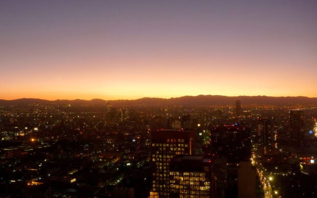 The Mexico City skyline shows glowing lights during sunset with mountains in the background, HD Desktop Wallpaper