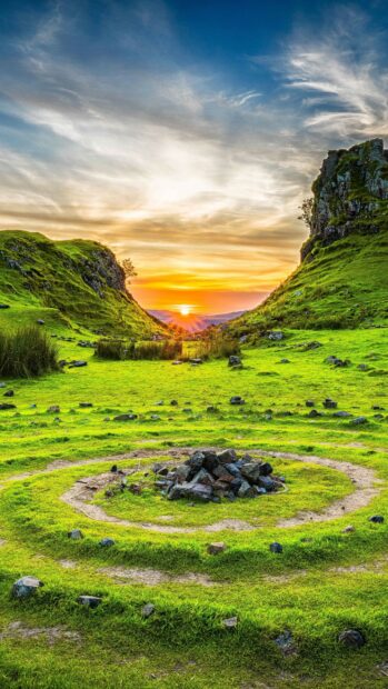 The United Kingdom Wallpapers show a beautiful sunset behind lush green hills and rocky formations, 2K Phone Wallpaper
