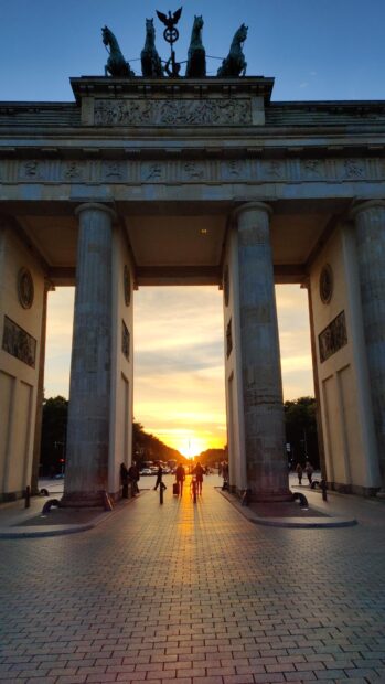 People walking through Brandenburg Gate Berlin at sunset with glowing sky, 4K Mobile Wallpaper
