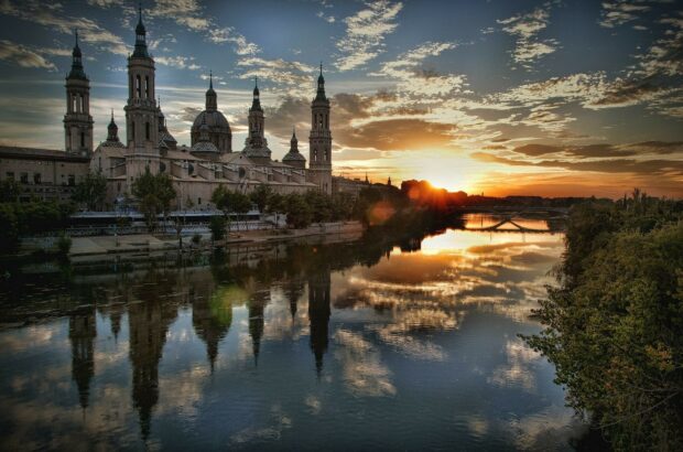 A beautiful sunset reflects on the river beside historic buildings in Spain with a cloudy sky, HD Desktop Wallpaper