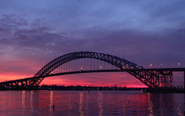 The Mississippi River flows beneath a large bridge during a stunning sunset with vibrant colors, HD Desktop Wallpaper