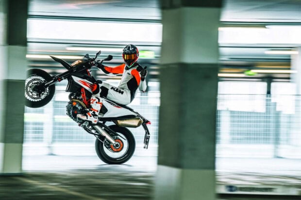 A rider performing a wheelie stunt on a supermoto motorcycle in a parking garage