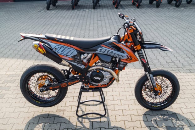 A supermoto motorcycle with orange and black details parked on a paved surface