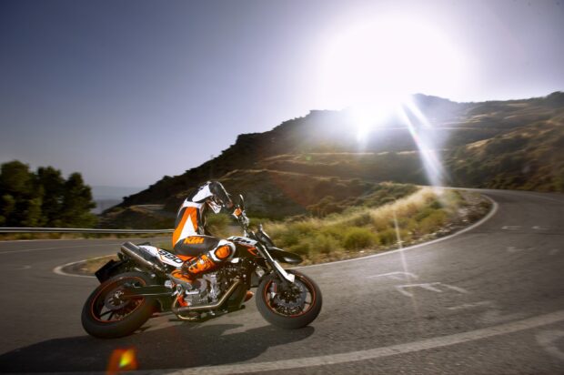 A rider on a supermoto leaning into a sharp mountain road corner at sunset