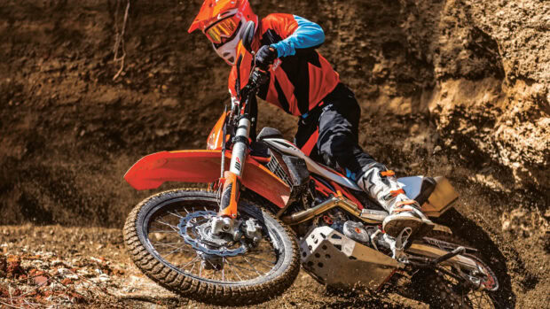 Rider wearing protective gear on supermoto bike cornering on dirt track