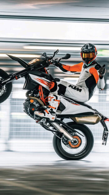 Rider performing a wheelie on a supermoto motorcycle wearing protective gear