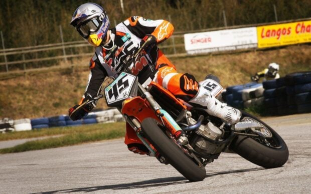 A rider in orange gear racing a supermoto bike with number 45 on a track