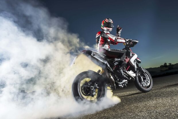 A supermoto rider performing a burnout on a high performance motorcycle on the road