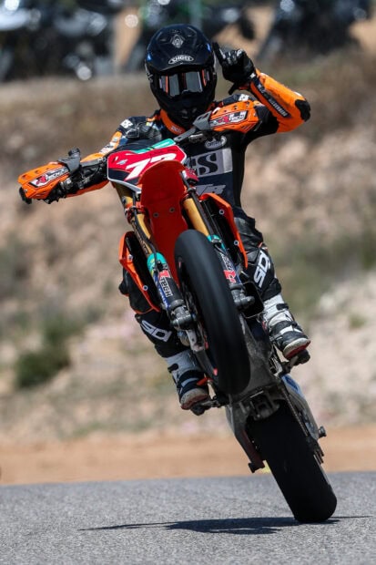 Male supermoto rider performing a wheelie on a race track in full gear