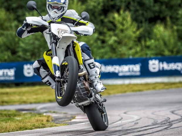 Rider performing a wheelie on a supermoto bike on a race track