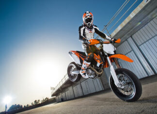 Supermoto rider performing a jump on an orange and white motocross bike outdoors