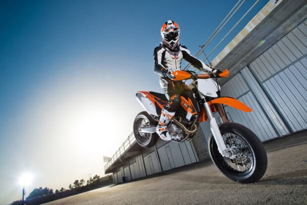 Supermoto rider performing a jump on an orange and white motocross bike outdoors