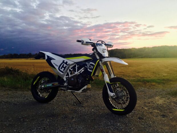 White and blue supermoto bike parked on a gravel road at sunset with a scenic field background