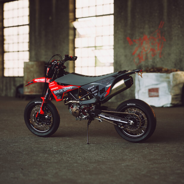 A red and black supermoto motorcycle standing in an industrial warehouse setting