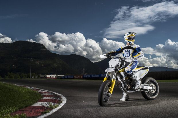 A rider on a supermoto bike wearing racing gear on a track with mountains in the background