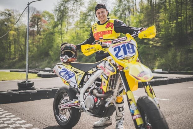 A smiling rider standing next to a yellow supermoto racing bike on a track