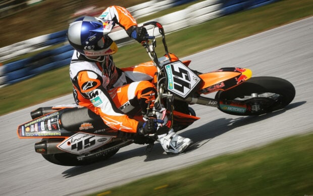 A supermoto rider in orange gear is racing around a track on a motorcycle with number 45