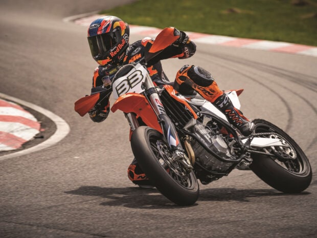 A supermoto rider leaning into a sharp turn on a race track with full gear and helmet